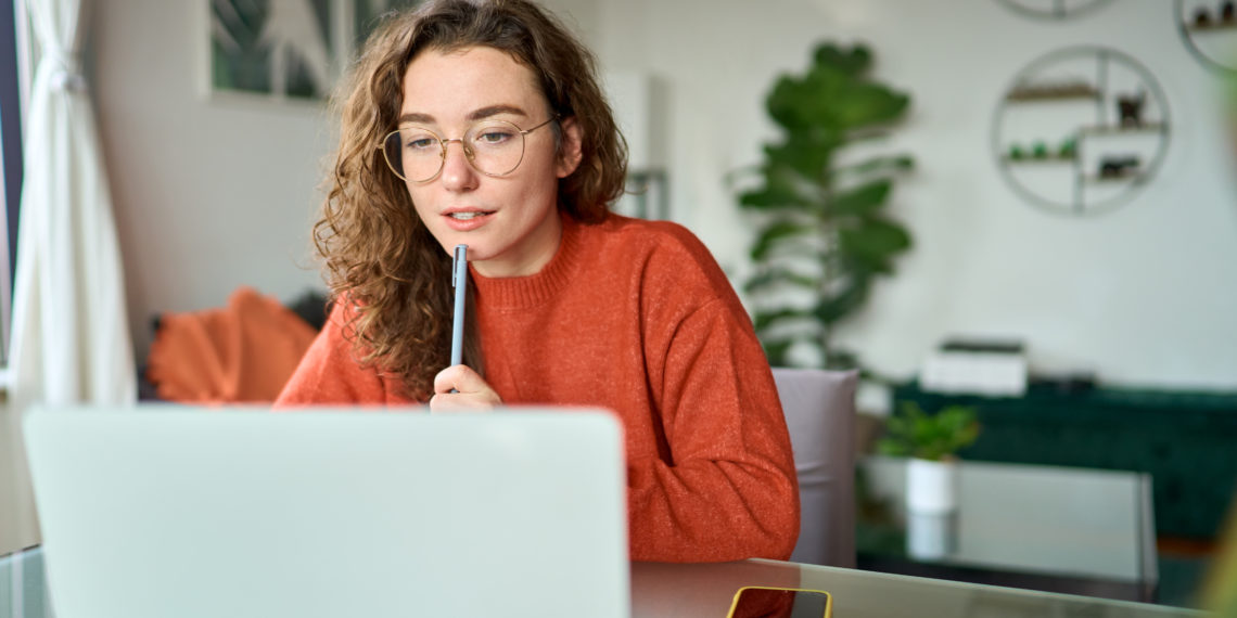 Young girl female student using laptop elearning or remote working at home office looking at computer watching webinar, learning training, studying online seminar or video calling for work meeting.