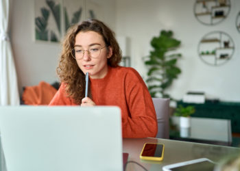 Young girl female student using laptop elearning or remote working at home office looking at computer watching webinar, learning training, studying online seminar or video calling for work meeting.