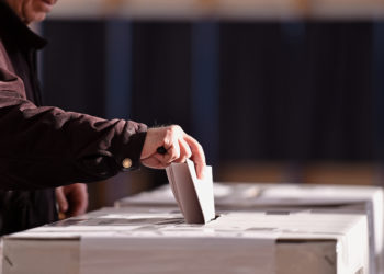 Hand of a person casting a vote into the ballot box during elections