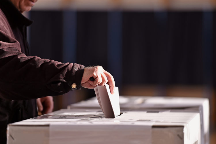 Hand of a person casting a vote into the ballot box during elections