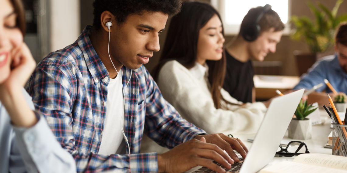 Student learning lessons in school library, making research on laptop and browse internet
