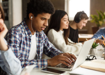 Student learning lessons in school library, making research on laptop and browse internet