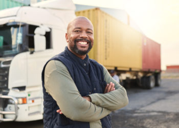 Delivery, container and happy truck driver moving industry cargo and freight at a shipping supply chain or warehouse. Smile, industrial and black man ready to transport ecommerce trade goods or stock.
