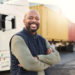 Delivery, container and happy truck driver moving industry cargo and freight at a shipping supply chain or warehouse. Smile, industrial and black man ready to transport ecommerce trade goods or stock.