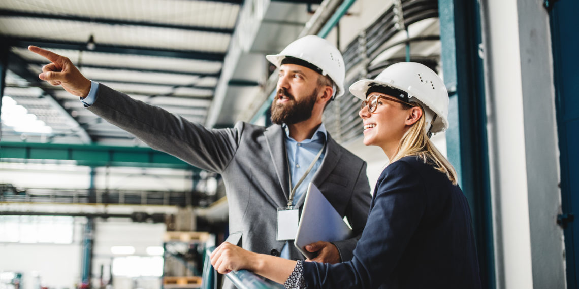 A portrait of a mature industrial man and woman engineer with tablet in a factory, working.
