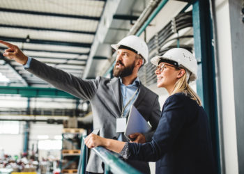 A portrait of a mature industrial man and woman engineer with tablet in a factory, working.