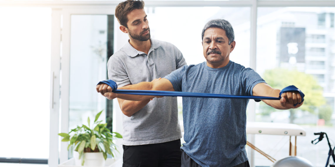 Physiotherapy, training and band with old man and doctor for stretching, rehabilitation and injury. Medical, healing and healthcare with physiotherapist and patient for consulting, help and fitness.