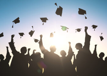 education, graduation and people concept - silhouettes of many happy students in gowns throwing mortarboards in air