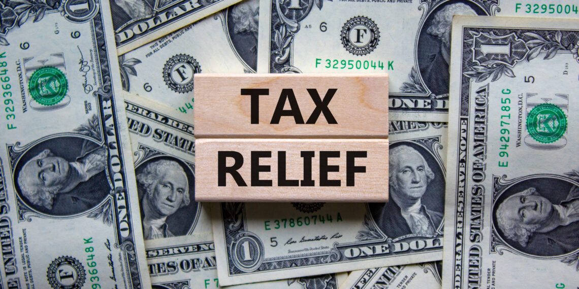 Tax relief symbol. Concept words 'tax relief' on wooden blocks on a beautiful background from dollar bills. Business and tax relief concept.