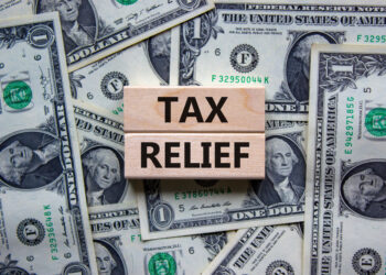 Tax relief symbol. Concept words 'tax relief' on wooden blocks on a beautiful background from dollar bills. Business and tax relief concept.