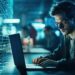 Cybercrime concept. A hacker, programmer, in a dark working space is hacking security, privacy, personnal information, with defocused many others working in his background