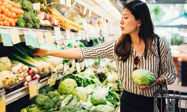 asian local woman buy vegetables and fruits in supermarket. young chinese lady holding green leaf vegetable and picking choosing green onion on cold open refrigerator. elegant female grocery shopping