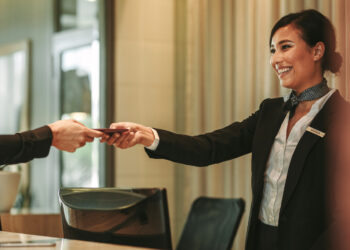 Smiling receptionist behind the hotel counter attending female guest. Concierge giving the documents to hotel guest.
