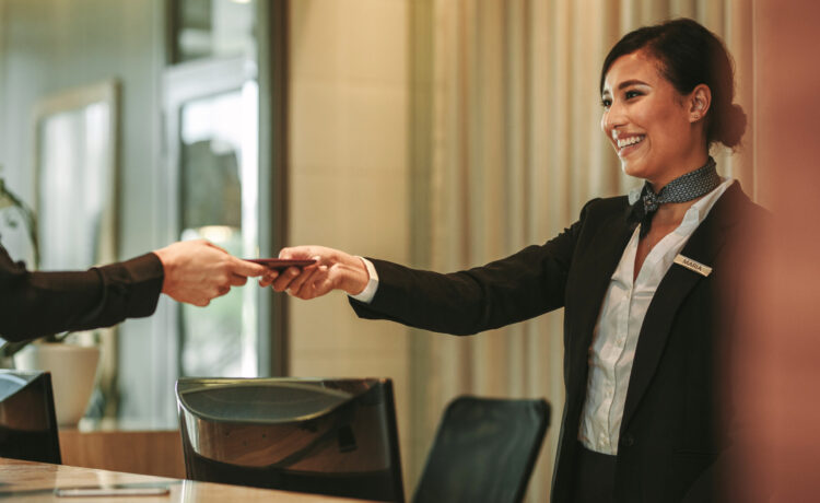 Smiling receptionist behind the hotel counter attending female guest. Concierge giving the documents to hotel guest.