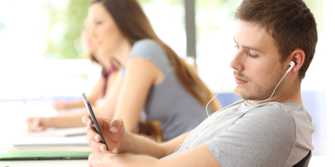 Bad student distracted listening to music sitting in a classroom