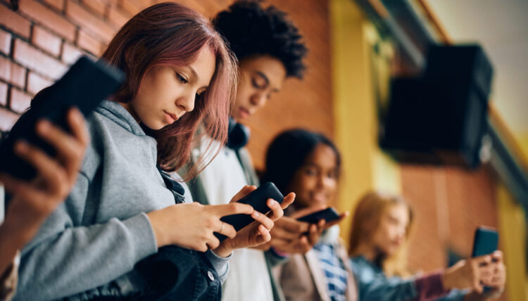 Group of teenagers using mobile phones in hallway at high school.