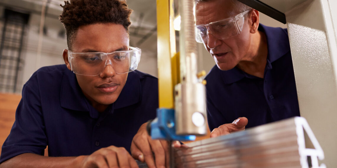 Carpenter Training Male Apprentice To Use Mechanized Saw