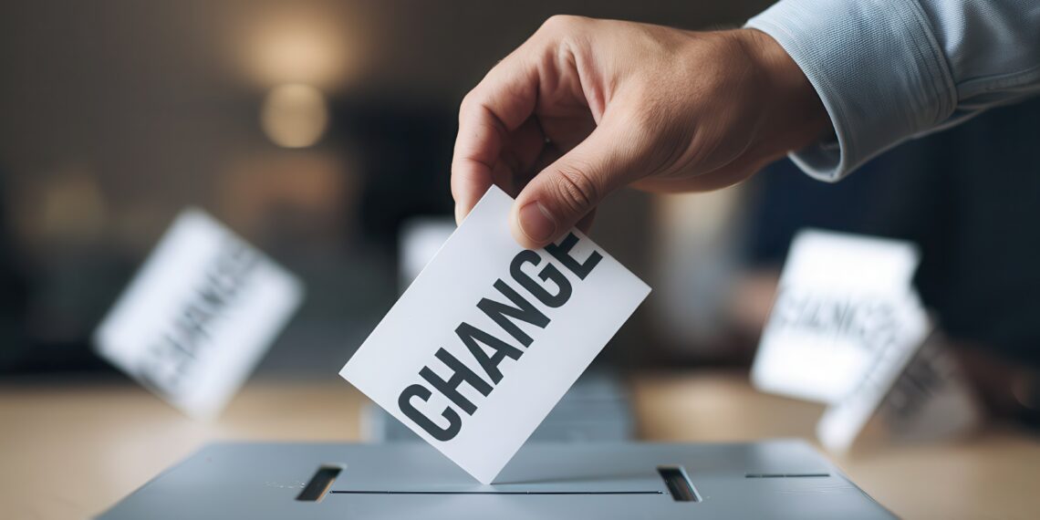 Hand casting a vote with the word CHANGE in a ballot box.