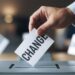 Hand casting a vote with the word CHANGE in a ballot box.