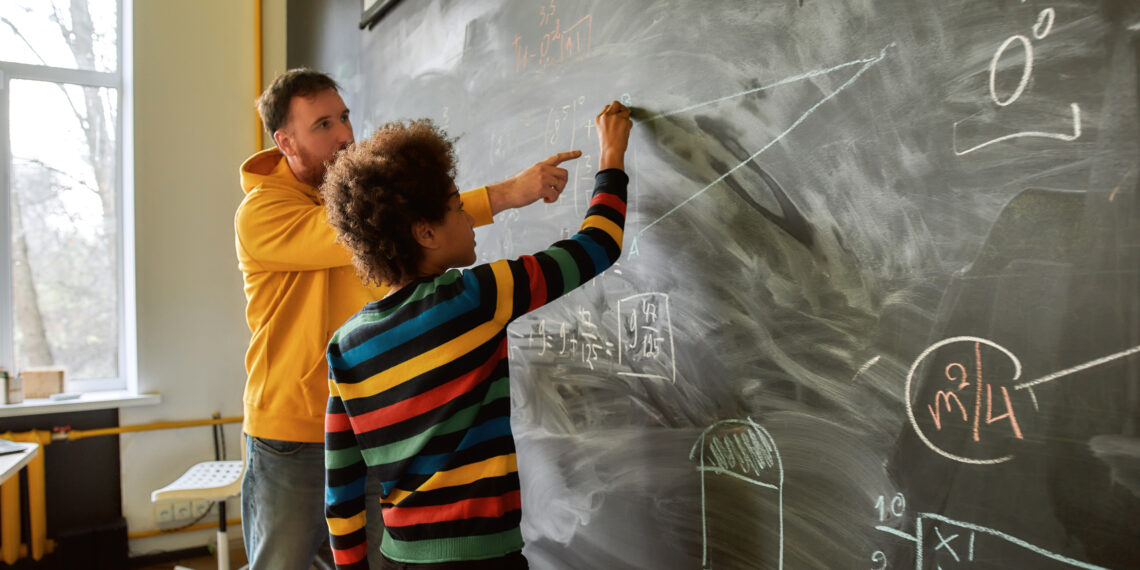 Young male science teacher explaining main rules and formulas in physics and mechanics for pupils. A boy is drawing on the blackboard. STEM disciplines, Math education concept tutoring tutor student teacher math