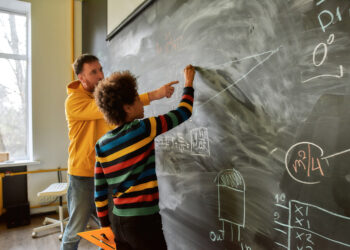 Young male science teacher explaining main rules and formulas in physics and mechanics for pupils. A boy is drawing on the blackboard. STEM disciplines, Math education concept tutoring tutor student teacher math