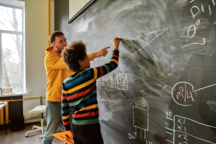Young male science teacher explaining main rules and formulas in physics and mechanics for pupils. A boy is drawing on the blackboard. STEM disciplines, Math education concept tutoring tutor student teacher math
