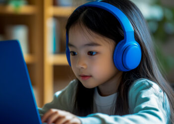A girl wearing a blue headset is using a laptop for an online school class.
