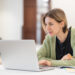 Smiling middle-aged woman studying online on laptop computer while sitting in classroom, doing second degree as mature student. Happy 45s female attending online professional development course