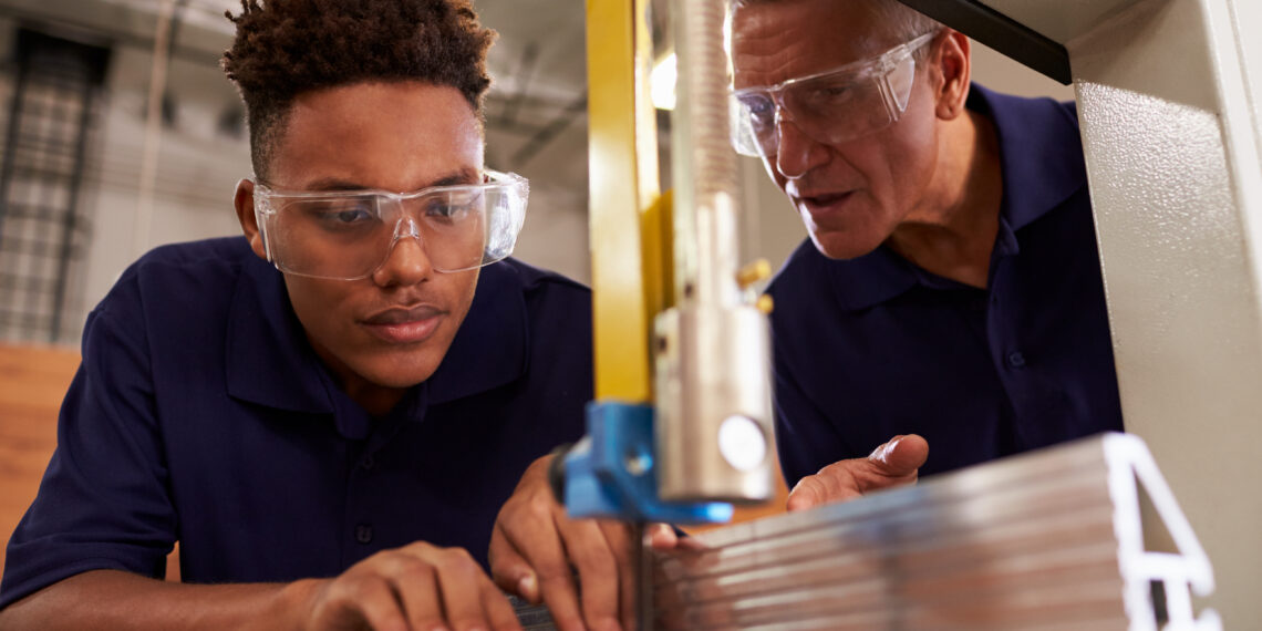 Carpenter Training Male Apprentice To Use Mechanized Saw