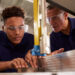 Carpenter Training Male Apprentice To Use Mechanized Saw