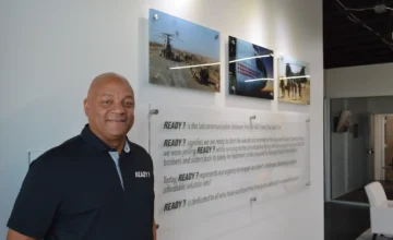 Maurice Compton standing beside the Ready 3 mission statement and military aviation photographs